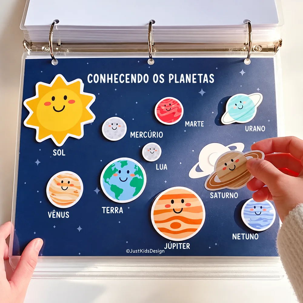 Página do sistema solar com planetas ilustrados e uma mão encaixando o recorte de Saturno